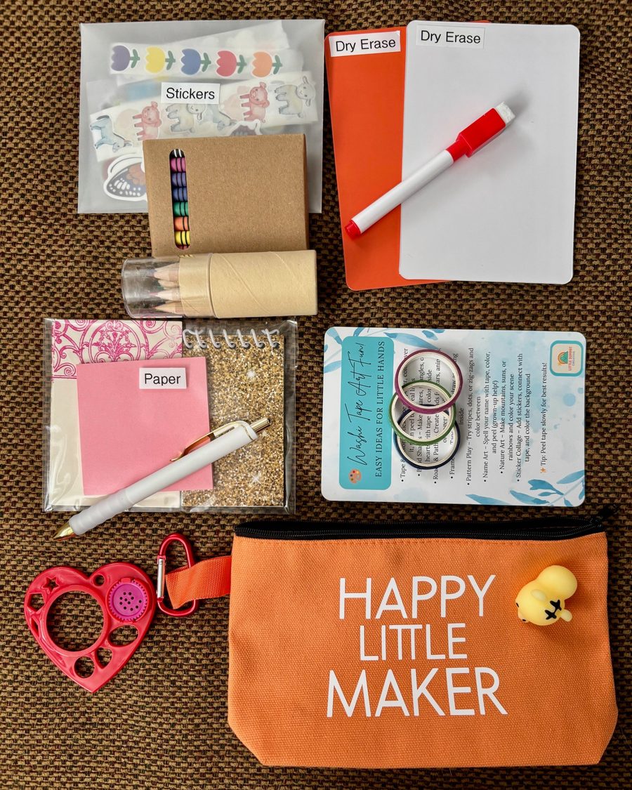 Orange Happy Little Maker pouch laid out with its contents: stickers, paper, colored pencils, crayons, washi tape, a dry-erase board and marker