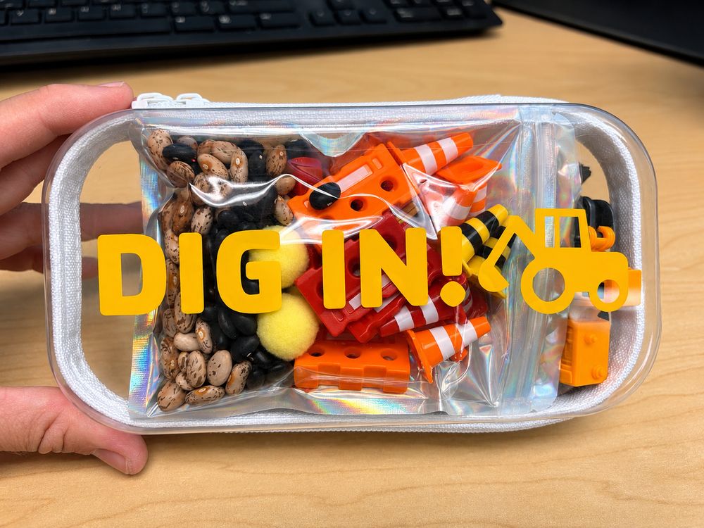 A clear zip case labeled Dig In! packed with dried beans, orange construction barriers, traffic cones and a toy digger