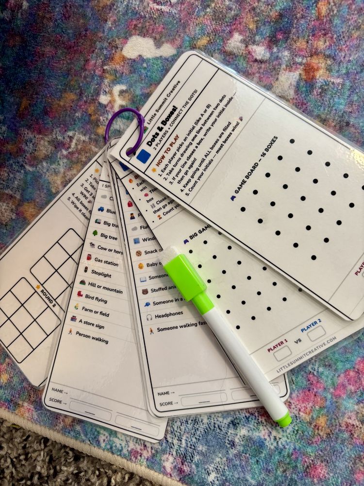 A fanned set of dry-erase game cards on a ring, including a dots-and-boxes board and a scavenger hunt list, with a green marker